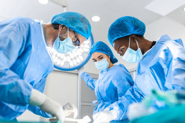 Preparation for the beginning of surgical operation with a cut. Group of surgeons at work in operating theater toned in blue. Medical team performing operation Preparation for the beginning of surgical operation with a cut. Group of surgeons at work in operating theater toned in blue. Medical team performing operation surgeon stock pictures, royalty-free photos & images