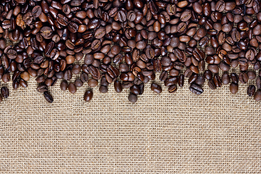Coffee beans on burlap background. Border design.