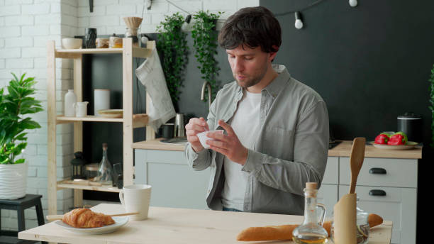 Young man eating yogurt in the kitchen at home stock photo