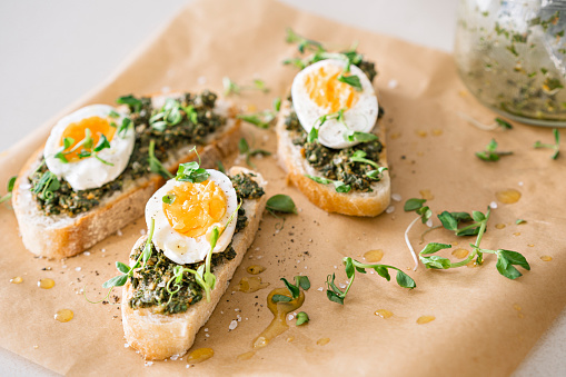 Sandwiches with egg, green pesto, micro greens and olive oil on paper on the table. Closeup on yellow backdrop. Vegetarian healthy natural food.