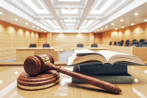 Interior of an empty courtroom with gavel, law books and sounding block on the desk.