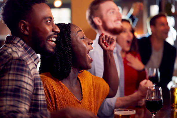 Group Of Excited Customers In Sports Bar Watching Sporting Event On Television Group Of Excited Customers In Sports Bar Watching Sporting Event On Television black people bar stock pictures, royalty-free photos & images