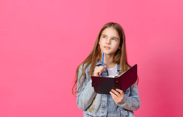ピンクの背景にノートとペンを持つ青いデニムジャケットで1かわいいペンシブ白い女の子10歳 - 10 11 years child human face female ストックフォトと画像