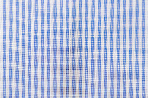 Striped textile pattern of a blue white business shirt. Fabric structure closeup of fashion clothing.