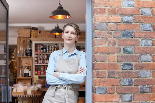 Portrait Of Female Owner Standing In Doorway Of Delicatessen Food Shop