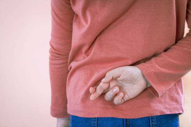 concetto sdraiato con una bambina che incrocia il dito dietro lo sfondo chiaro con spazio di copia. buon primo aprile. - sdraiarsi foto e immagini stock