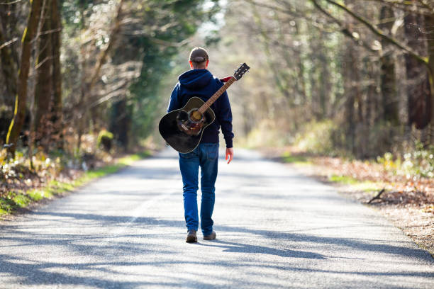 istock Man walking on country road with guitar on his back 1306124102