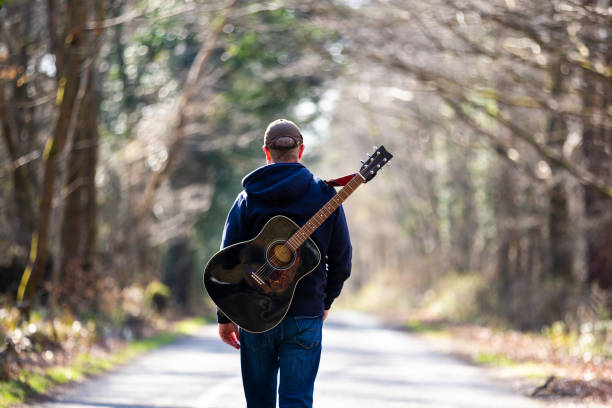istock Man walking on country road with guitar on his back 1306124104