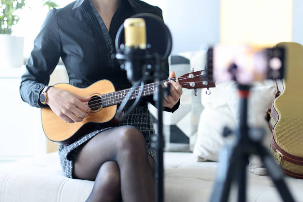Woman plays ukulele, and records on smartphone Woman plays ukulele, and records on smartphone. Learning to play the guitar on video courses concept dubstep photos stock pictures, royalty-free photos & images