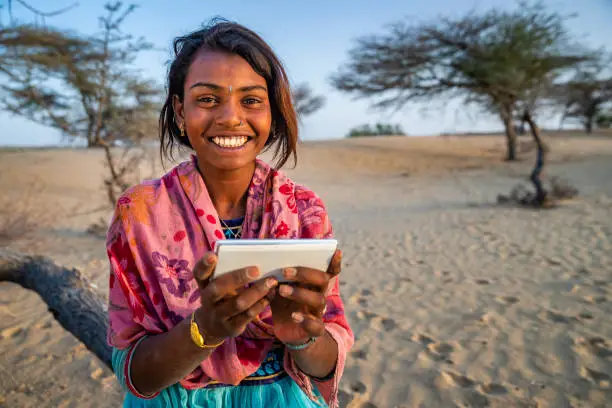 Happy Gypsy Indian girl using mobile phone in desert village, Thar Desert, Rajasthan, India.