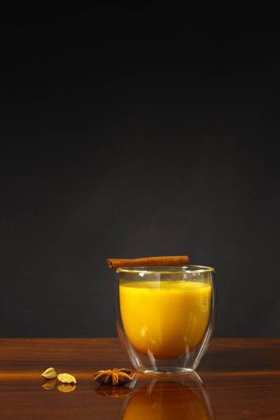 A glass of golden moon milk with turmeric and a stick of cinnamon. Hot drink with spices. Close-up, vertically with space stock photo