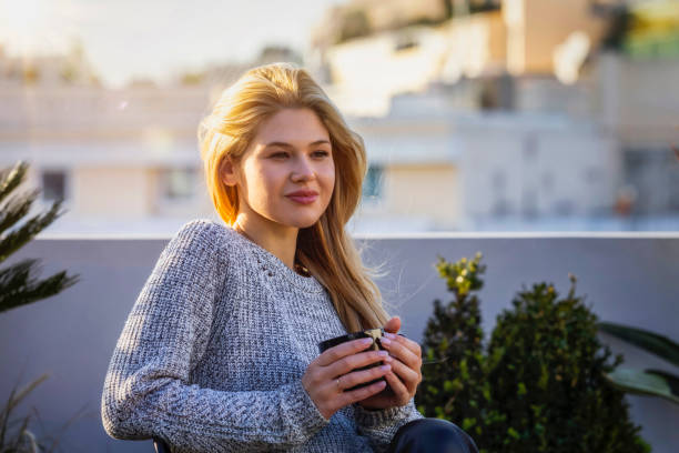 una donna bionda si siede sulla terrazza e si gode il suo caffè mattutino - balcony women patio coffee foto e immagini stock