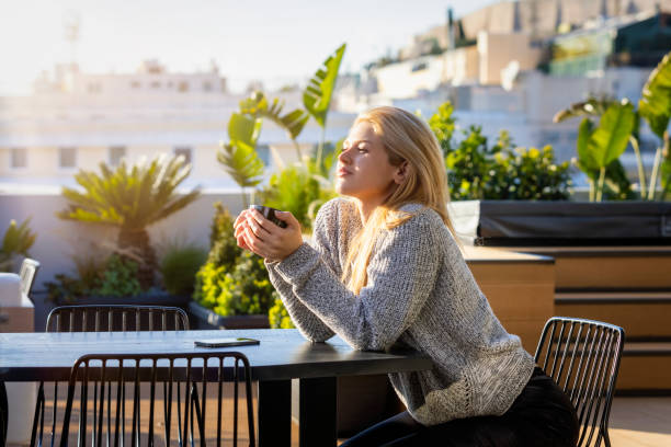 una donna bionda si gode il suo caffè mattutino all'aperto sulla terrazza - balcony women patio coffee foto e immagini stock