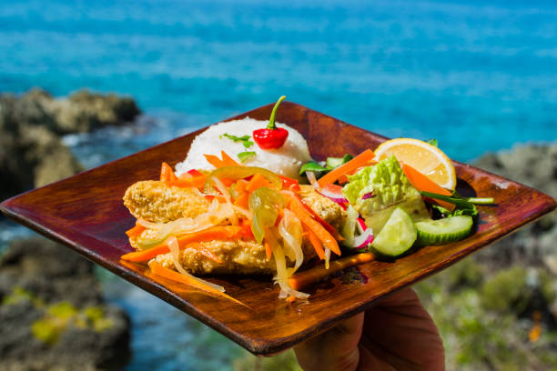 escovitch de poisson servi avec du riz blanc et salade verte sur une plaque en bois au bord de l’océan - cayman islands photos et images de collection