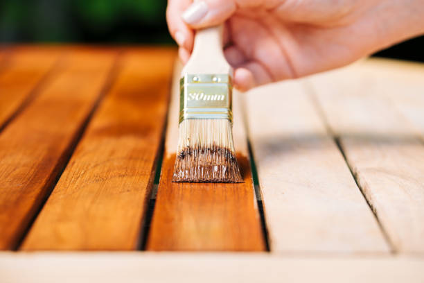 mão segurando um pincel aplicando tinta verniz em uma mesa de jardim de madeira - pintura e cuidado com madeira com óleo - brushing paint house painter human hand - fotografias e filmes do acervo