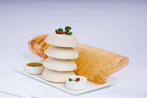 Ghee roast  Dosa and Idlii Ghee roast  Dosa and Idlii, south indian main breakfast item which is beautifully arranged in a white plate lined with banana leaf  and curry as sambar and chutney on white background. thosai stock pictures, royalty-free photos & images