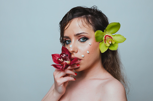 Beauty portrait of a young woman with brown hair holding orchid flowers against a white background