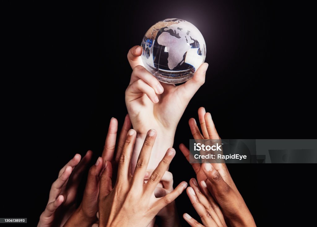 Group of many diverse hands reaches up for a crystal globe of the world, Africa facing the camera Many hands trying to get hold of a world globe made of glass. Globe - Navigational Equipment Stock Photo