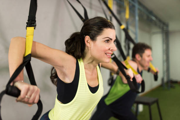 Attractive 40-year-old woman and man performs suspension training in gym Attractive 40-year-old woman and man performs suspension training in gym suspension training stock pictures, royalty-free photos & images