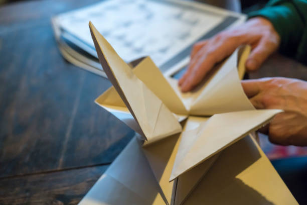 Close up on male hands making large origami from white paper on dark wooden table after instructions.
