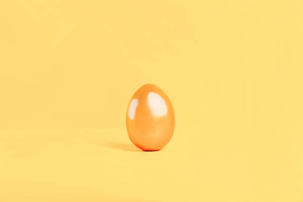 istock Painted egg in gold color standing on yellow background, an expensive egg, expensive food. Preparing for the religious holiday Easter, painting eggs for the event 1306144584