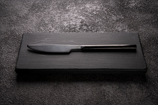a black table knife on a wooden podium. stylish minimalistic still life.