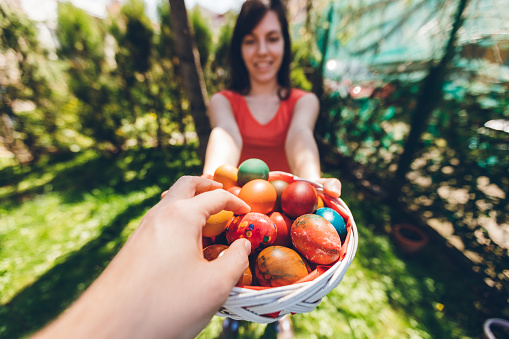 Man's hand is taking an Easter egg from a basket held by young woman.