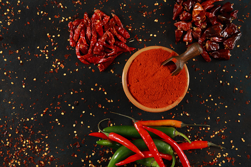 Fresh and dried chilli peppers and powders scattered on black background stone