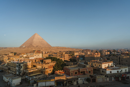 Giza, Cairo, Egypt - September 30, 2021: Pyramid of Cheops, the largest of the Egyptian pyramids. Tourists walk and take pictures near her against the background of the blue sky.