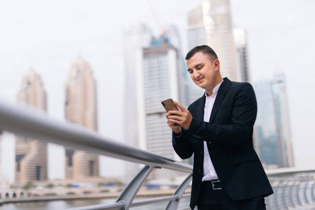 istock Young handsome businessman reading text message on cell phone on skyscrapers background 1306154672