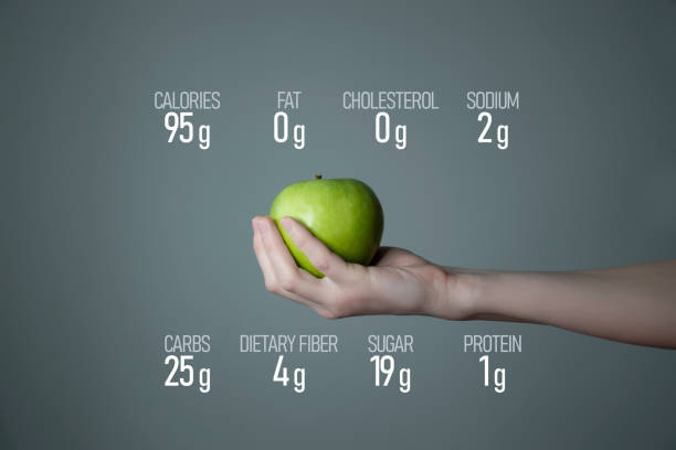 Woman`s hand holding green apple, nutrition facts on grey background.
