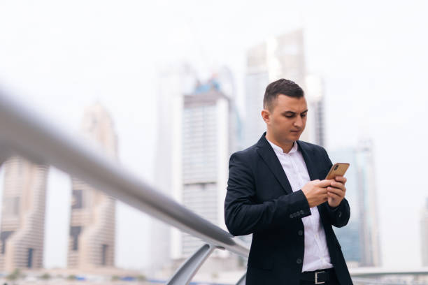 istock Young handsome businessman reading text message on cell phone on skyscrapers background 1306156603