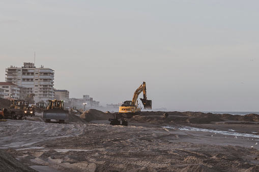Indialantic, Florida, USA - February 11, 2021: Earth moving equipment, including bulldozers and an excavator, work at sunset on a beach reclamation project in Brevard County, Florida, distributing sand pumped in from offshore.