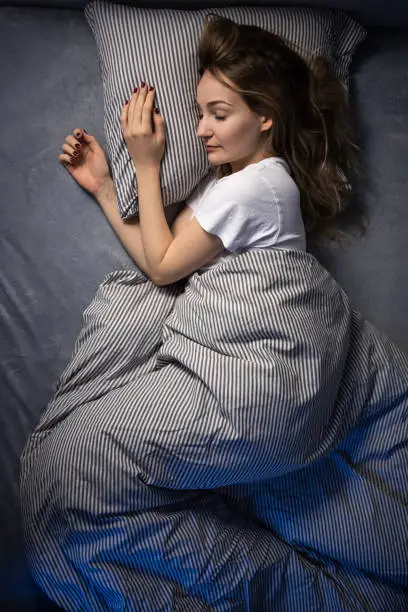 Pretty, young woman sleeping in her bed late in the morning on a weekend - compensating for the lack of sleep