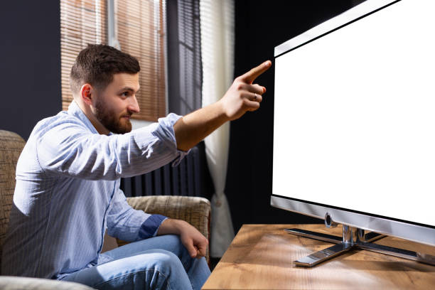 istock Great idea. Delighted freelancer raising his forefinger out and wrinkling forehead while having plan. Watching with attention mock up white tv screen, space for ads, publicity and text 1306165171