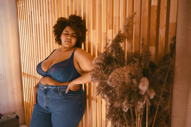 Beautiful stylish curvy oversize African black woman with afro hair posing in bra and jeans on wooden eco friendly background, body imperfection, body acceptance, body positive and diversity concept.. stock photo