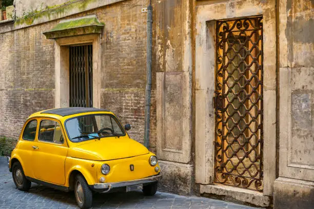 A 1969 Fiat 500 parked in an alley in the historic center of Rome, in the Spanish Steps district. This vintage car is a symbol of Italian design and industry also present in the MoMA museum in New York. Image in high definition format.