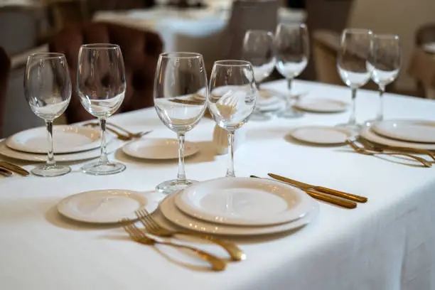 Chic and elegant, gold-plated cutlery and white plates, table setting with empty plates. Luxury restaurant, preparation for the celebration. Close-up on a served place.
