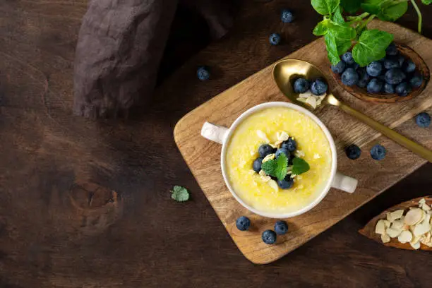 Polenta dish with blueberries and almonds. Corn porridge in a ceramic plate on the brown wooden kitchen table. Cream-soup with polenta. Healthy Vegetarian food. Top view