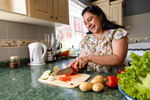 feliz mamá hispana cocinando alimentos saludables - mujer madura cortando verduras frescas en su cocina - mujer haciendo ensalada saludable - salad course fotografías e imágenes de stock