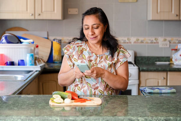 maman hispanique recherchant des recettes sur son téléphone-femme prenant des photos de la salade organique saine de sa femme au foyer prenant des photos tout en cuisinant - grandmother women one person senior adult photos et images de collection