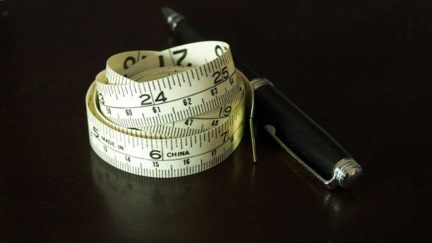 istock Rolled measuring tape and a fountain pen on a semi-reflective dark surface 1306178167