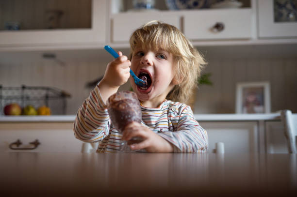 istock Small boy with dirty mouth indoors in kitchen at home, eating pudding. 1306180824