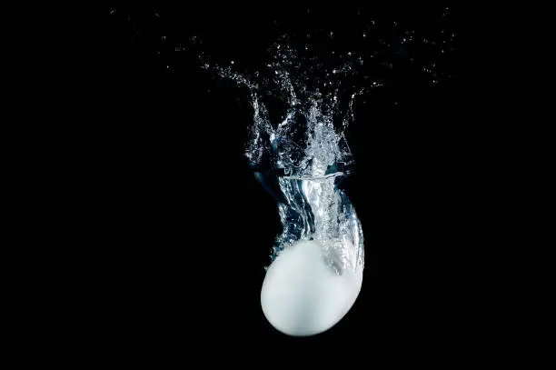 Fresh egg dropped into water with splashes isolated on black background