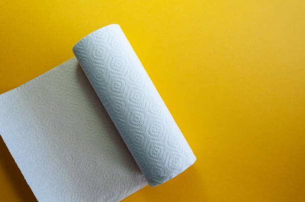 Paper Towel Roll on the bushing on yellow background. Kitchen paper on a table indoors.