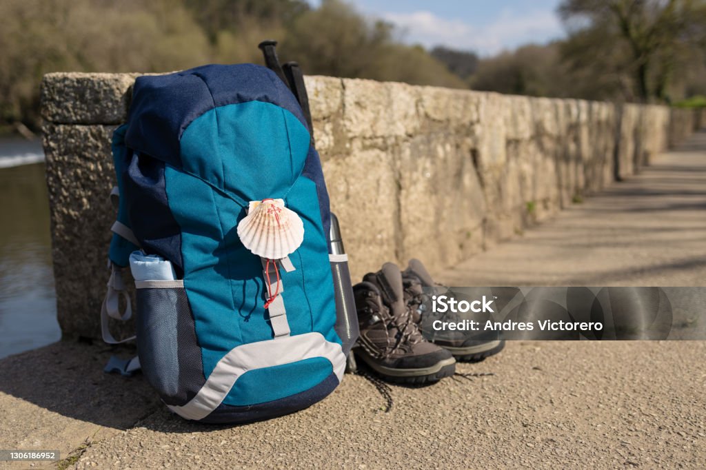 Backpack with seashell symbol of Camino de Santiago Backpack with seashell symbol of Camino de Santiago, trekking boots and poles leaning on stone wall. Pilgrimage to Santiago de Compostela. Copy space Santiago de Compostela Stock Photo