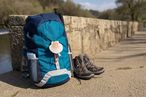 Backpack with seashell symbol of Camino de Santiago Backpack with seashell symbol of Camino de Santiago, trekking boots and poles leaning on stone wall. Pilgrimage to Santiago de Compostela. Copy space santiago de compostela stock pictures, royalty-free photos & images