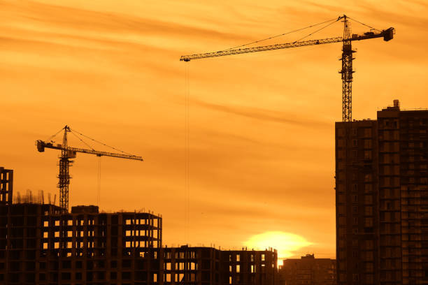 Construction site with new buildings and cranes at dusk evening yellow cloudy sky background, sunlight, back light