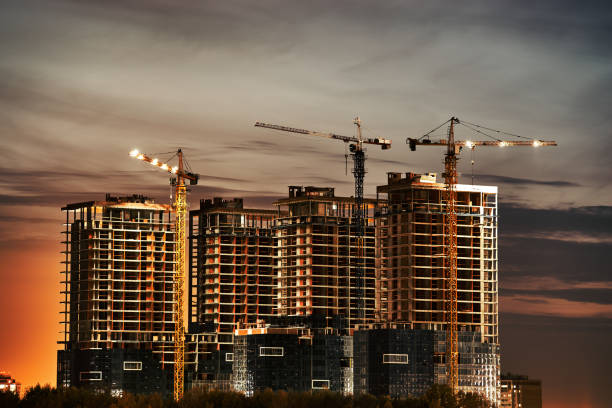 istock Construction site with new buildings and cranes at evening blue yellow cloudy sky background. Night evening light 1306187005