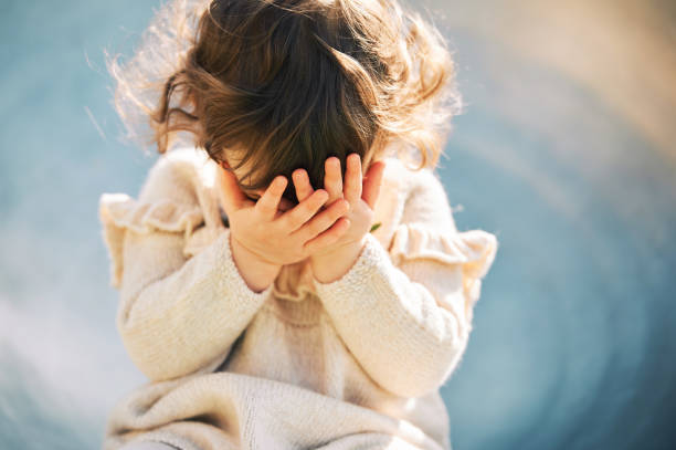 Portrait of adorable little girl hiding face with hands stock photo